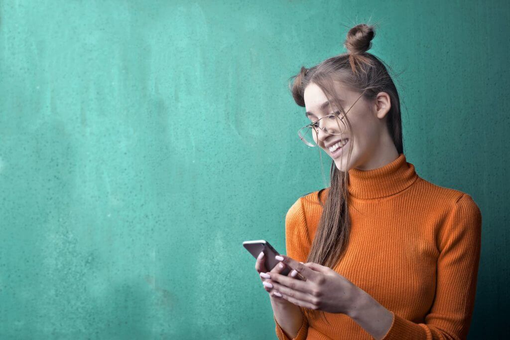 woman in orange turtleneck sweater holding black smartphone